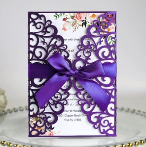 Detail of laser-cut purple lace wedding invitation with ribbon bow on glass tray