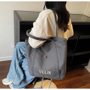 Détail du sac fourre-tout en toile grise avec broderie blanche TELN porté à l'épaule
