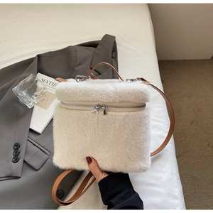 Flat lay of a plush white faux fur handbag with brown leather straps on a white bed