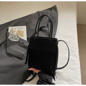 Détail d'un sac seau noir à franges avec bandoulière et finition en similicuir