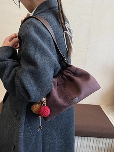 Sac à bandoulière en daim marron avec plis et breloques porté sur manteau gris
