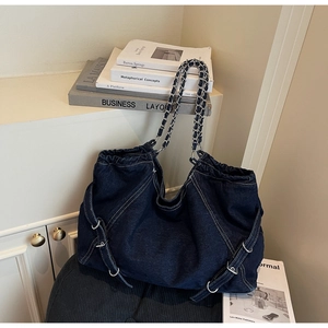 Detailed macro of dark denim tote bag featuring white stitching and metallic silver accents