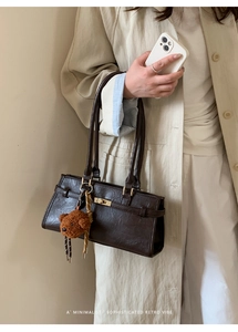 Detail of dark brown leather handbag with gold twist lock and cute plush bear charm
