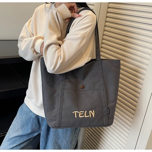 Détail du sac cabas en toile avec broderie TELN et poche avant porté à l'épaule