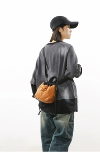 Detail of quilted bright orange nylon bucket bag with black adjustable shoulder strap
