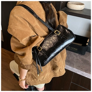 Détail d'un sac sous le bras noir brillant plissé porté par un mannequin chic