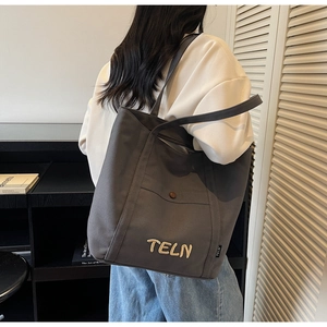 Détail du logo brodé et de la poche à pression sur ce grand sac fourre-tout en toile gris foncé