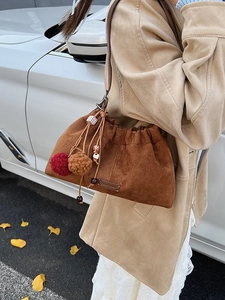 Sac seau en daim marron avec cordon de serrage et pompons porté par un mannequin en automne