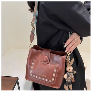 Close-up of brown bucket bag with lychee texture and ethnic style woven wide shoulder strap
