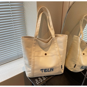 Vue détaillée du sac cabas en toile blanc cassé avec poche latérale et broderie marine