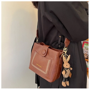 Detail of vintage brown leather bucket bag with creative rabbit charm and adjustable strap