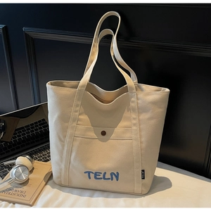 Détail du sac fourre-tout en toile crème avec broderie bleue et poche avant à bouton-pression