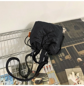 Detail of black quilted nylon bucket bag featuring drawstring closure and orange woven tag