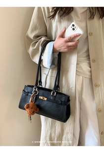 Detail of a minimalist black handbag with gold rotary lock and brown plush bear charm