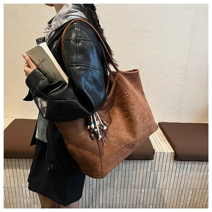 Détail d'un sac cabas en daim marron avec des clous dorés et un pendentif à franges