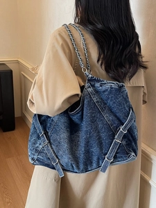 Large blue denim tote bag with vintage wash and metal chain strap worn on shoulder