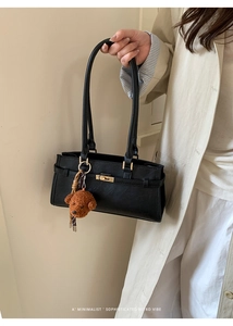 Detail of black leather handbag with gold twist lock and a cute plush bear charm