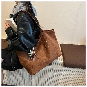 Close-up of brown suede tote bag with golden studs and colorful tassel keychain detail