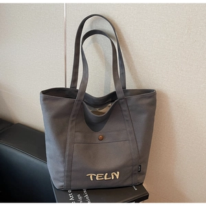 Détail du sac cabas en toile gris foncé avec poche avant, bouton marron et logo TELN
