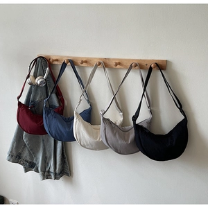 Collection of minimalist crescent crossbody bags in five colors hanging on wooden hooks