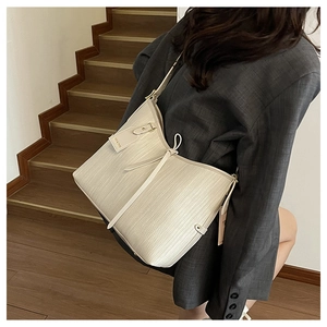Dettaglio della borsa tote beige intrecciata con nappa e tracolla indossata da una modella