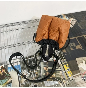 Detail of brown quilted bucket bag featuring black drawstring and wide fabric strap