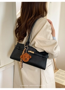 Detail shot of a black leather shoulder bag with gold twist lock and a cute bear charm