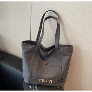 Détail des poignées renforcées et de la broderie blanche sur un sac fourre-tout en toile grise