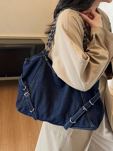 Large dark blue denim tote bag with chain strap and buckles on beige trench coat