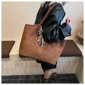 Close-up of brown suede tote bag with metal rivets and decorative tassel detail