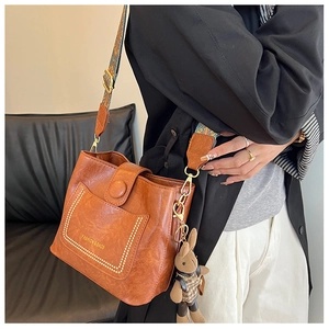 Close-up of brown bucket bag featuring vintage texture, embroidery strap, and a rabbit charm