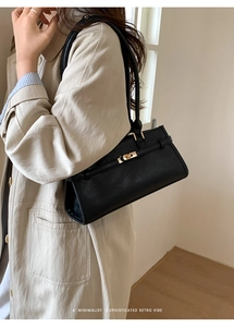 Detailed view of black minimalist handbag featuring gold turn-lock closure and leather texture