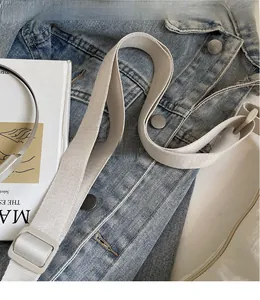 Detail of adjustable woven shoulder strap in beige with resin buckle on denim fabric