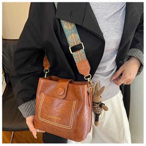 Detail of vintage brown bucket bag with patterned strap and rabbit charm worn by model