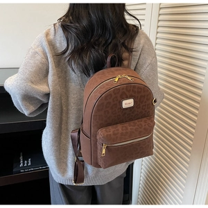 Detailed view of brown leopard print backpack with gold metal zippers on a model
