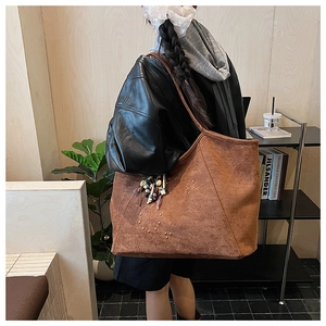 Détail du sac cabas en daim marron avec rivets métalliques et breloque en perles