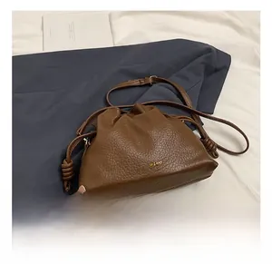 Detail of dark brown pebble leather crossbody bucket bag with gold logo on grey fabric