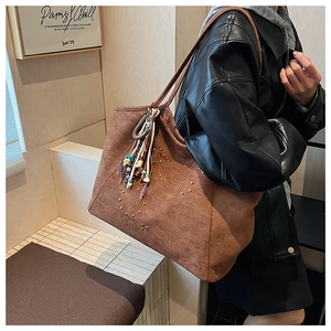 Détail du sac cabas en daim marron avec motifs de cœurs en rivets et pompon ethnique