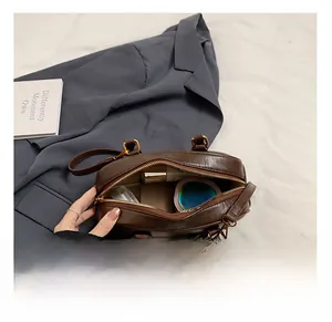 Détail de l'intérieur du sac bowling en cuir marron avec cosmétiques et fermeture éclair