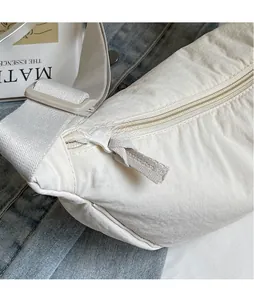Detail of off-white dumpling crossbody bag with extended fabric zipper pull on magazines