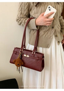 Detail of dark red leather shoulder bag with gold twist lock and cute plush bear charm
