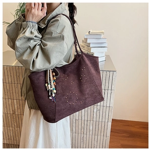 Detail of burgundy suede tote bag with golden rivets and bohemian tassel charm accessory