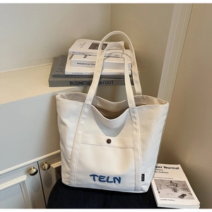 Détail du sac cabas en toile blanche avec broderie bleue et étiquette de marque latérale