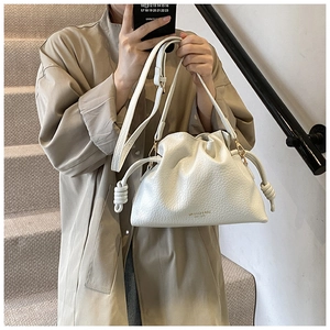 Detailed texture of white ruched bucket bag with gold brand logo and drawstring closure
