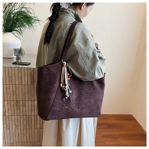 Détail du cabas en daim prune avec rivets métalliques et pendentif à pompon bohème