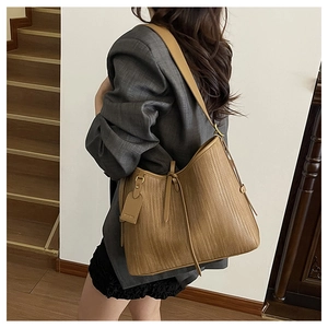 Dettaglio borsa tote intrecciata color cuoio con etichetta in pelle e nappa su donna