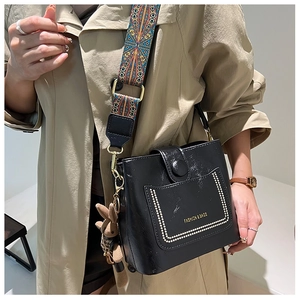 Detail of black bucket bag featuring golden rivet studs and ethnic pattern wide strap