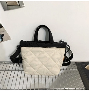 Detail of quilted nylon bucket bag featuring cream finish and black contrast handles
