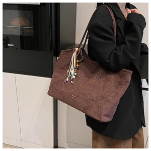 Détail d'un sac cabas en daim marron avec clous dorés et pendentif pompon coloré