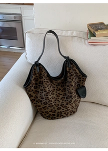 Gros plan du sac cabas en daim léopard avec anse en cuir noir posé sur un canapé beige